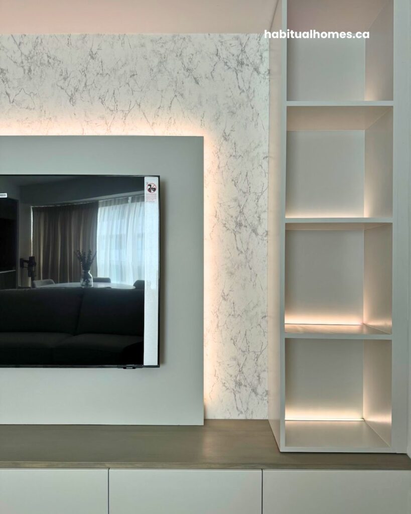 Close-up of custom media wall with marble-look wallpaper, integrated LED lighting around TV, and open built-in shelves in a Bloor East Toronto condo